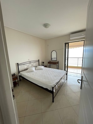 A bedroom with a bed, a bedside table, a mirror, and a window with a balcony.