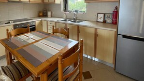 Une cuisine dotée de meubles en bois, d’un réfrigérateur en acier inoxydable, d’une table à manger avec des chaises et d’une fenêtre laissant entrer la lumière naturelle.