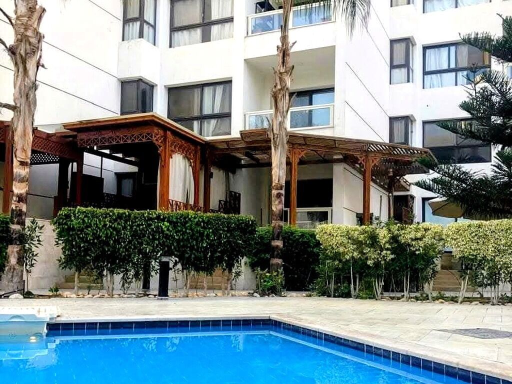 A hotel with a swimming pool, a covered outdoor area, and a building with multiple balconies.