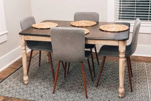 Una mesa de comedor con cuatro sillas, un mantel negro y protectores de mesa tejidos.