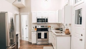 A modern kitchen with white cabinetry, stainless steel appliances, and a wooden floor. - 115 yr old Historic Heffner House in Downtown Rogers (Rogers)