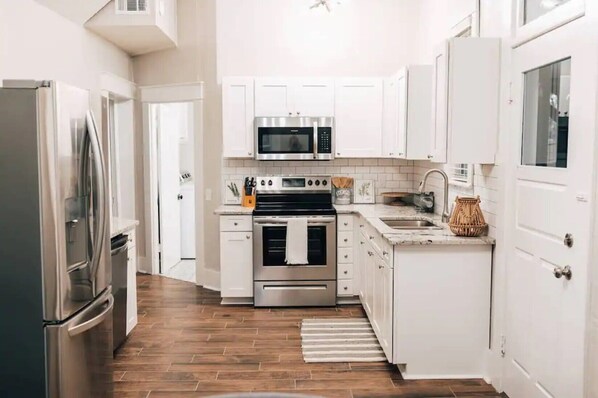 Una cocina moderna con armarios blancos, electrodomésticos de acero inoxidable y piso de madera.