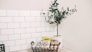 A kitchen counter with a white tiled backsplash, a small potted plant, and a basket containing a box of Skinny Pop cereal, a jar of peanut butter, and a container of peanut butter. - 115 yr old Historic Heffner House in Downtown Rogers (Rogers)