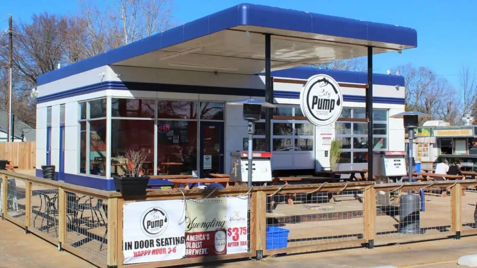 Un camión de comida con decoración azul y blanca, que muestra un logo 'Pump' y un letrero anunciando 'Comedor Interior' y 'La Cervecera Más Antigua de Estados Unidos' con una oferta especial.