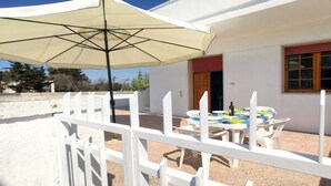 Une maison blanche avec un patio, une table entourée de chaises et un grand parasol.