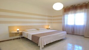 Une chambre à coucher avec un lit, deux tables de chevet, une commode et une fenêtre avec des rideaux.