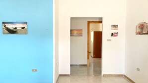 Un couloir avec un mur bleu sur la gauche, une porte en bois au fond, et un petit tableau sur le mur de droite.