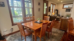 Un coin repas avec une table et des chaises en bois, un tapis à motifs et de grandes fenêtres donnant sur la forêt.