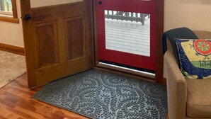 Une porte en bois avec un cadre rouge, un paillasson, une horloge et des œuvres d’art accrochées au mur.