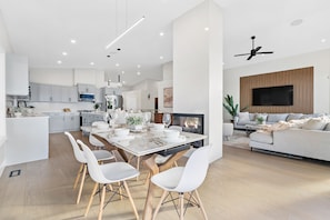 A modern kitchen with white cabinetry, a dining area with a white table and chairs, and a living room with a sofa and TV.