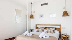 Un lit bien fait, avec une tête de lit en bois, deux tables de chevet et une plante en pot.