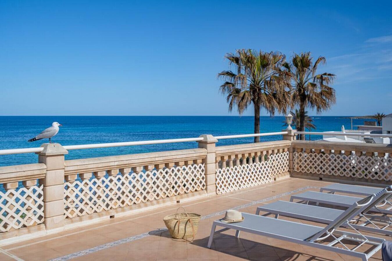 A balcony with a white lattice railing, lounge chairs, a hat, and a basket.