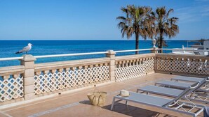 Un balcon doté d’une balustrade blanche en treillis, de chaises longues, d’un chapeau et d’un panier.