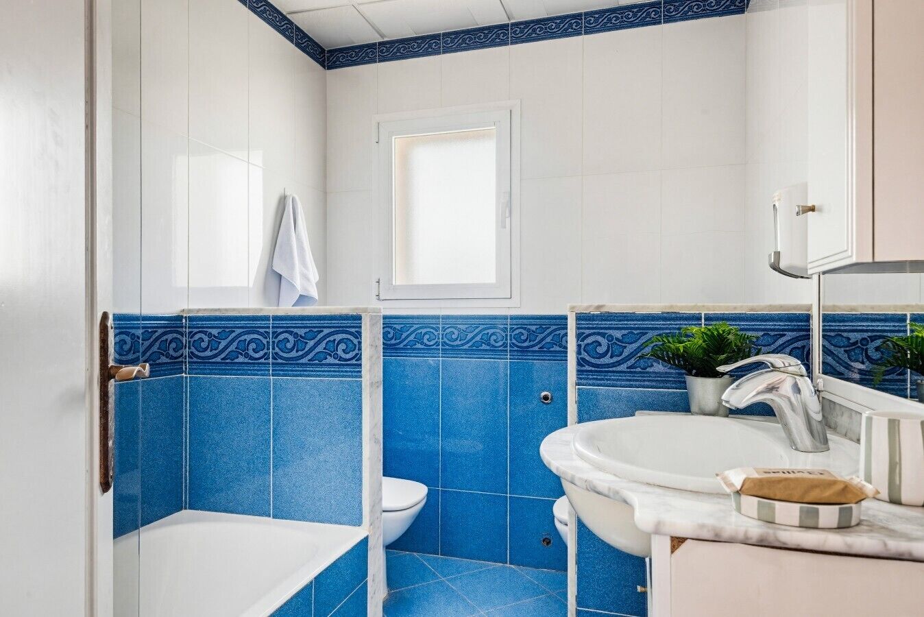 Um banheiro com azulejos azuis e brancos, vaso sanitário branco, pia branca e chuveiro.