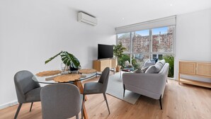 Una sala moderna con una mesa de comedor de vidrio, sillas grises, un sofá gris y un televisor.