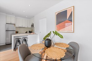 Relax in this stylish living space with a glass-top dining table, comfortable chairs, and a vibrant abstract art piece.