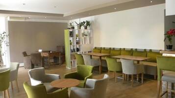A modern dining area with green and white chairs, wooden tables, and a green sofa.