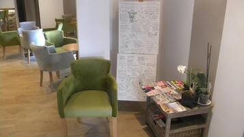 A seating area with green chairs, a small table with magazines, and a whiteboard with handwritten notes.