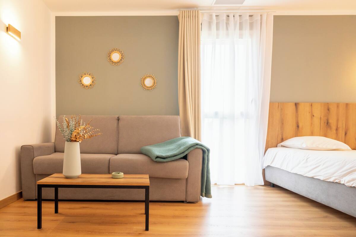 Una habitación con sofá, cama, mesa de centro y elementos decorativos en la pared.