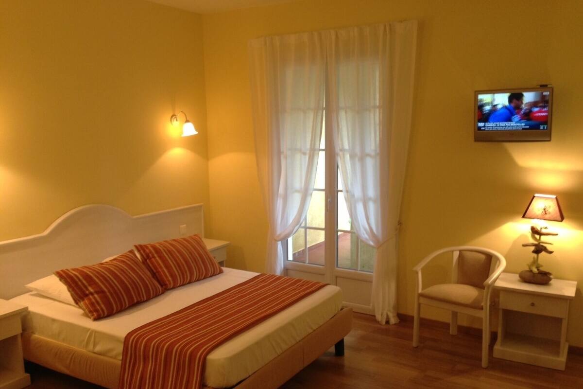 Una habitación de hotel con cama, una silla, televisor y lámpara.