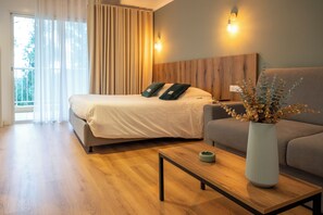 A modern hotel room with a bed, a sofa, a wooden coffee table, and a vase with dried flowers.