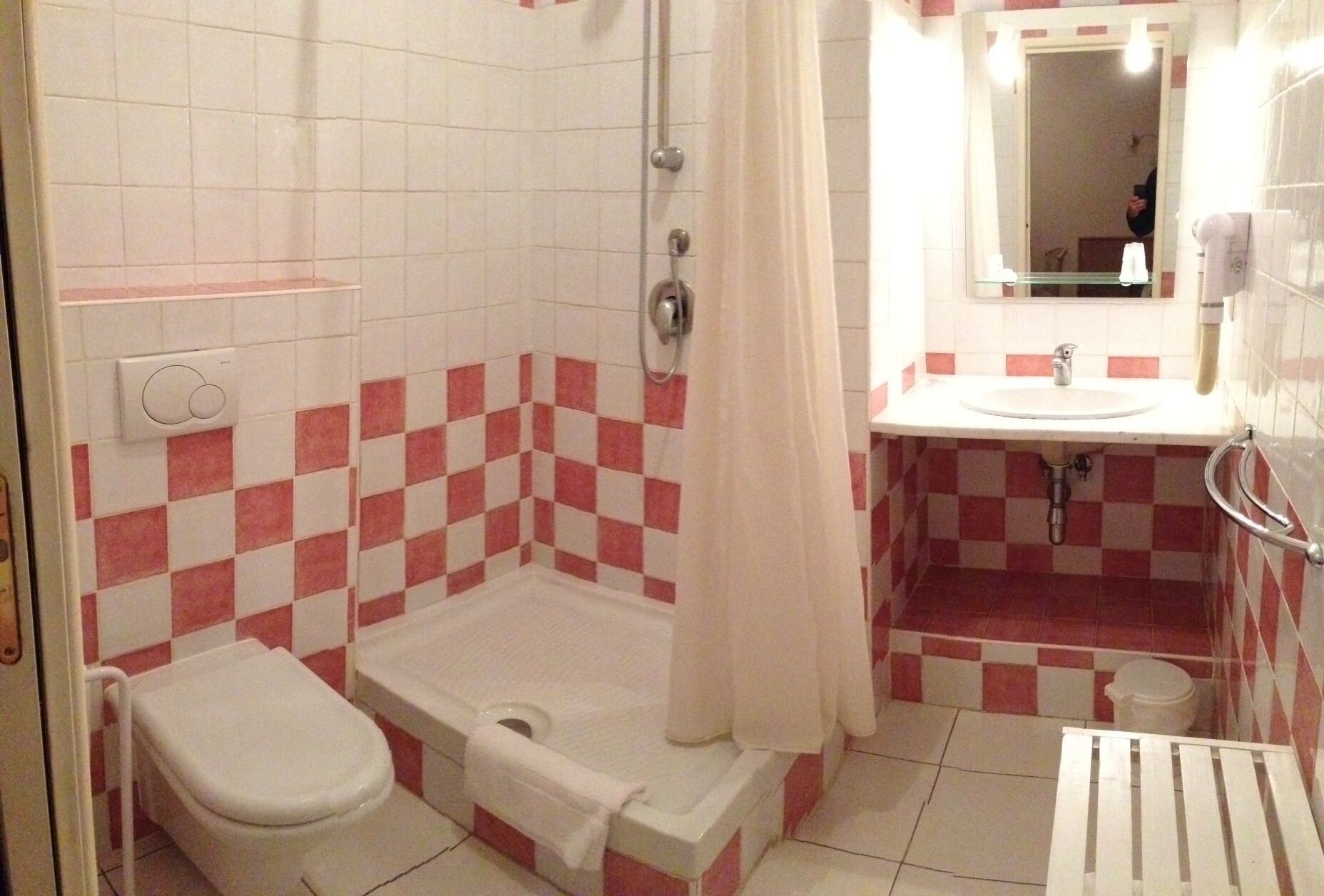 Une salle de bain avec un carrelage à motifs à carreaux, une douche, des toilettes et un lavabo avec un miroir au-dessus.