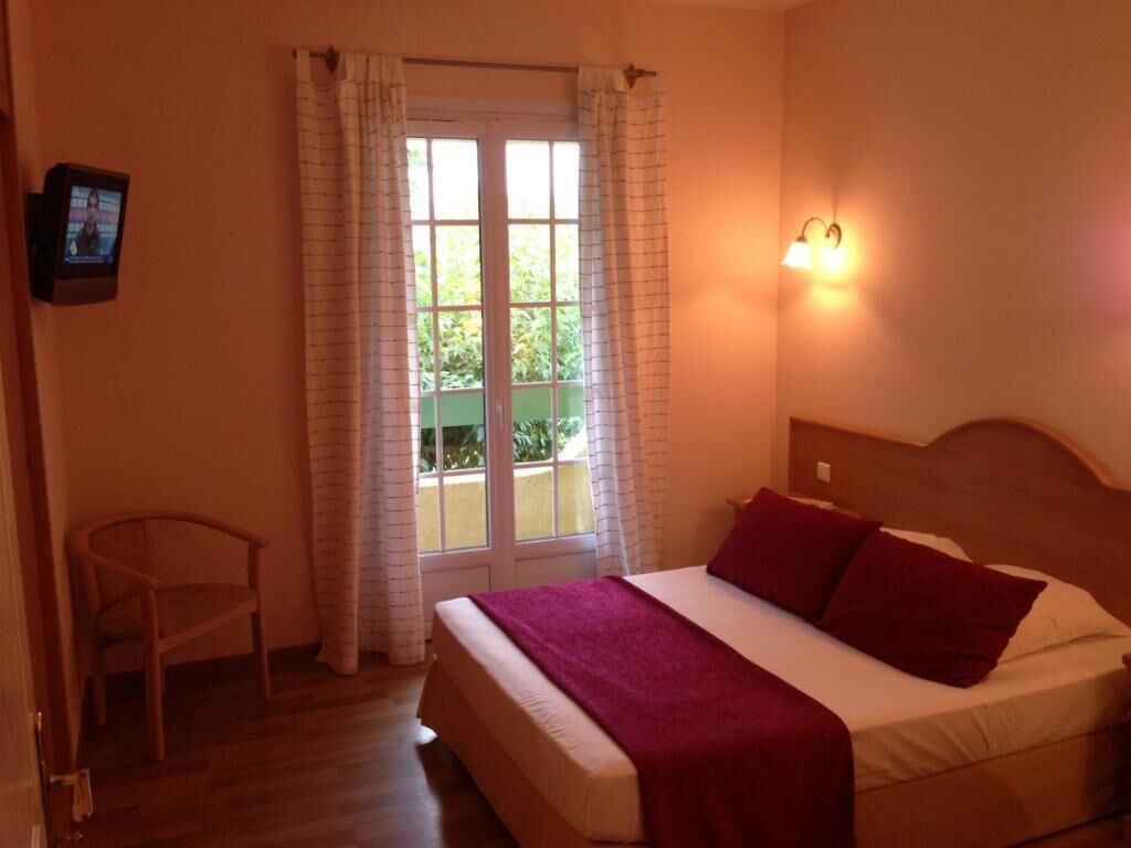 Quarto com cama, cadeira, televisão e janela com cortinas.