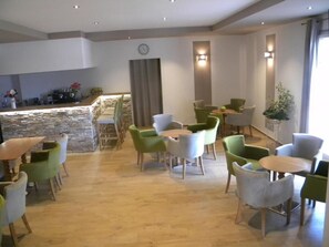 Un vestíbulo de hotel con mostrador de piedra, sillas verdes y blancas, y suelo de madera.