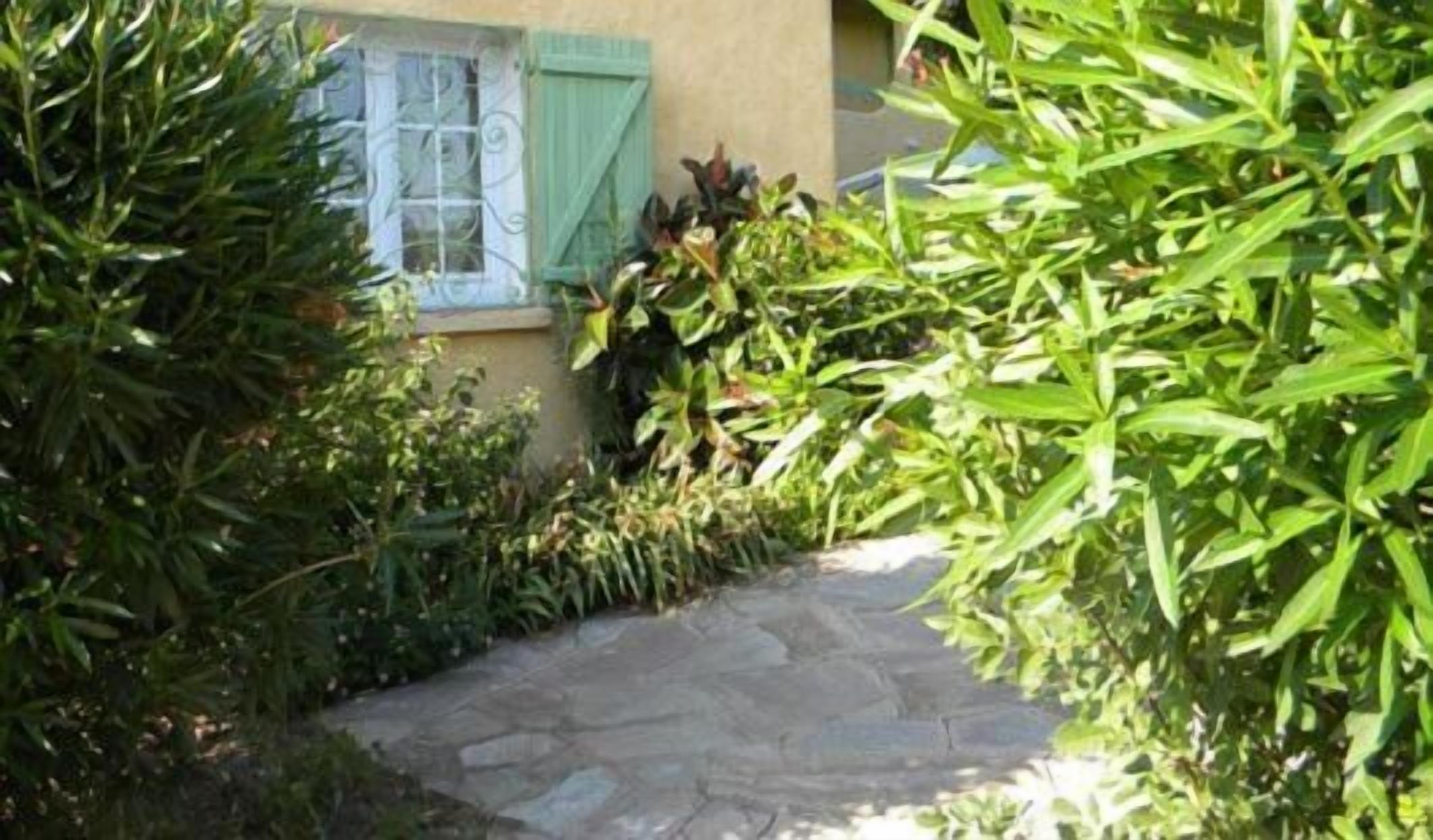 A stone pathway leading to a building with a window and green shutters.