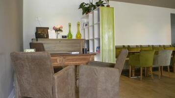 A modern living room with a wooden coffee table, two armchairs, a sofa, and a dining area with a green-striped partition.