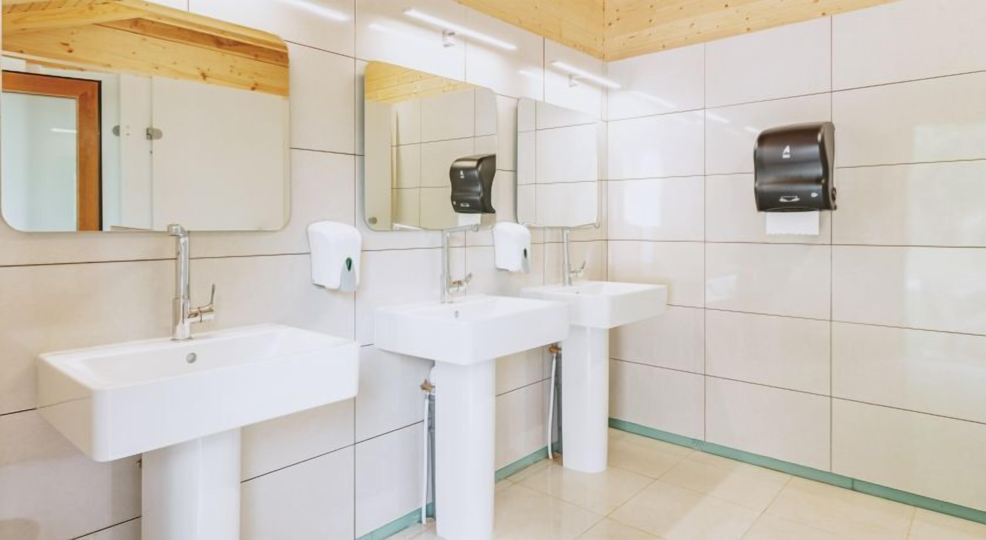 A restroom with three sinks, a mirror, and hand soap dispensers.