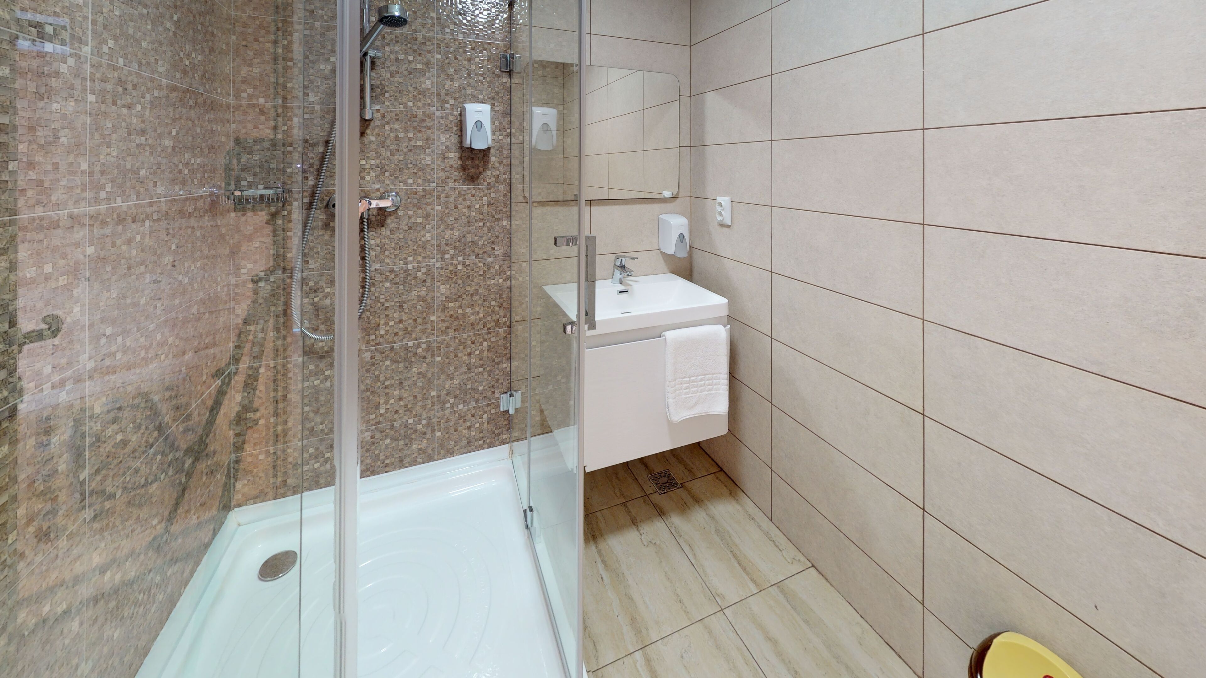 A modern bathroom with a glass shower enclosure, a white sink, and a tiled floor.