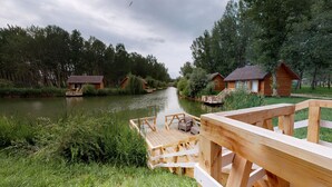 A riverside wooden cabin with a deck, surrounded by lush greenery and a calm river. - Zaga Zaga Sat (Cosmesti)