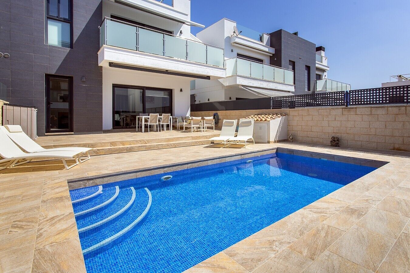 Ein moderner Poolbereich mit rechteckigem Pool, Liegestühlen und einem Essbereich mit Gartenmöbeln.