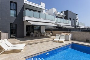 A modern two-story house with a swimming pool, outdoor seating, and a covered patio area.