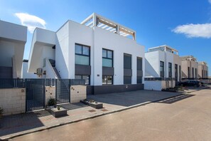 A modern residential building with a flat roof, large windows, and a gated entrance.