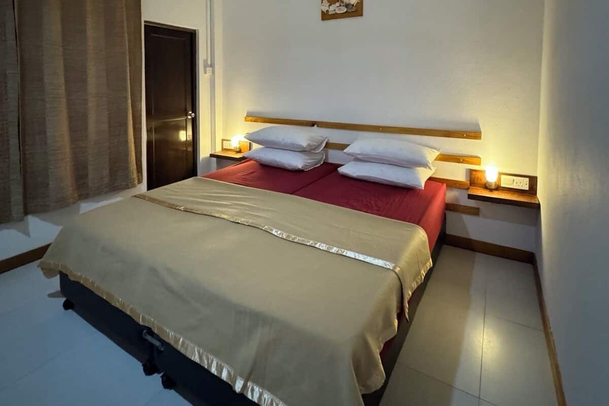 A hotel room with a bed, curtains, a ceiling fan, a wall clock, and a small table.