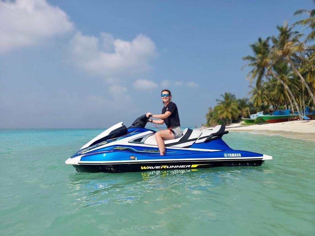 En person på en Yamaha Waverunner jetski på klart turkis vand med en strand og palmer i baggrunden.