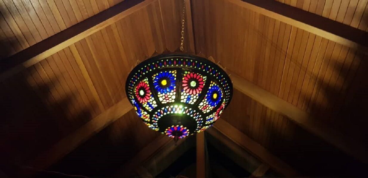 A chandelier with a stained glass design hanging from a wooden ceiling.