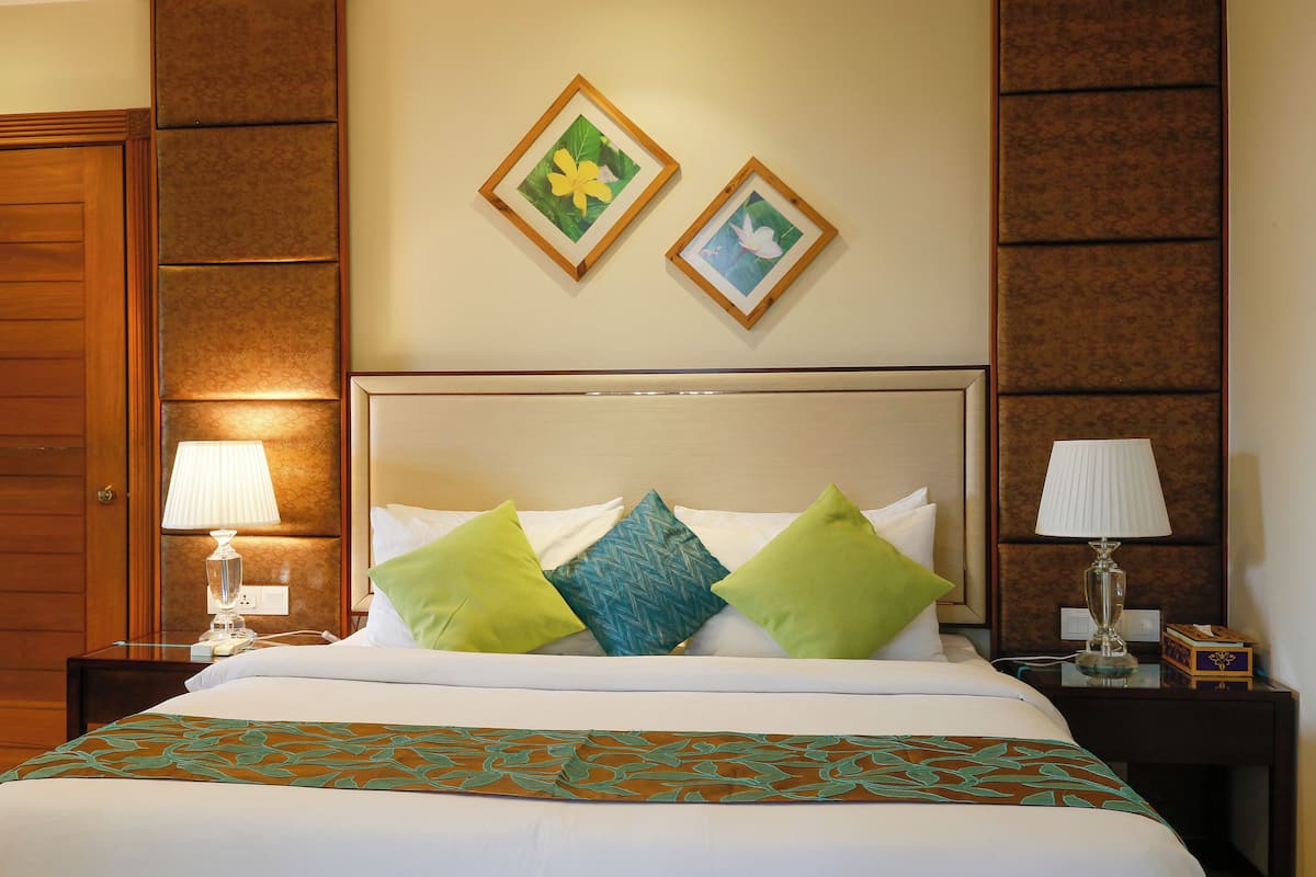 A hotel room with a large bed, two nightstands, a wooden door, and two framed pictures on the wall.