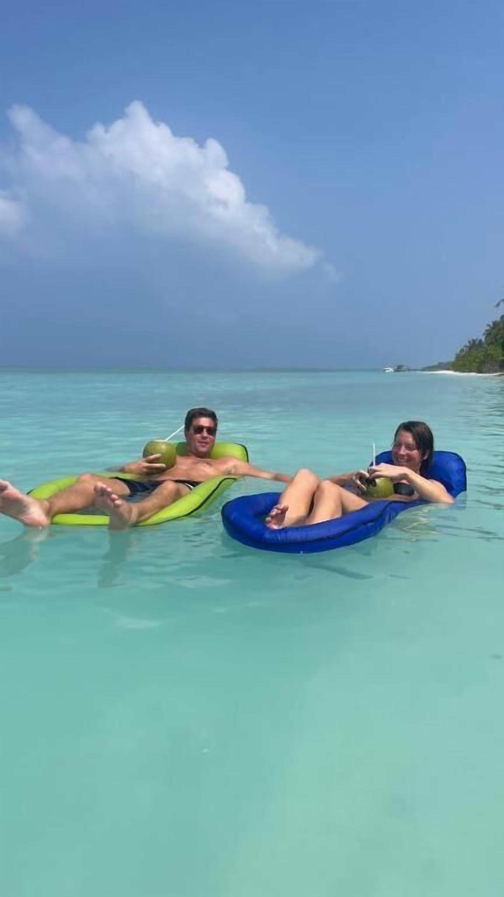 Dos personas flotando en un mar azul cristalino con una isla tropical al fondo.