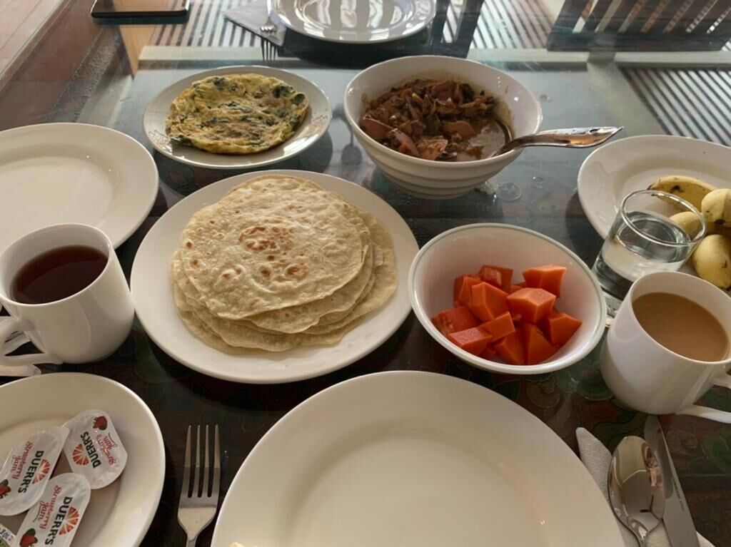 A table set with various dishes including flatbreads, a bowl of meat, and a bowl of cubed vegetables, along with cups and utensils.