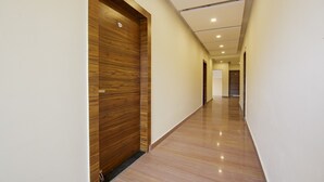 A long, narrow hallway with wooden doors on one side and a polished floor. - Treebo Grand Vista - 63A (Noida)