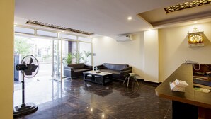 A modern lobby with a sofa, coffee table, and a fan. - Treebo Grand Vista - 63A (Noida)