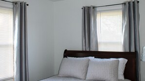 Een slaapkamer met een bed, gordijnen, een plafondlamp en een raam.