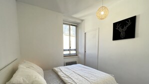 A bedroom with a single bed, a window, a door, and a wall-mounted artwork. - Haut du village, T2 + alcôve 5p. (Cauterets)