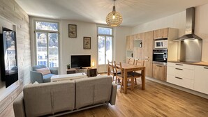 A modern living room with a sofa, dining table, and kitchen area with wooden cabinets and appliances. - Haut du village, T2 + alcôve 5p. (Cauterets)