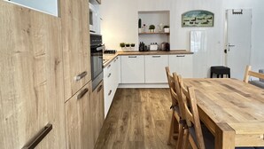 A modern kitchen with wooden cabinets, a built-in oven, and a dining area with a wooden table and chairs. - Haut du village, T2 + alcôve 5p. (Cauterets)