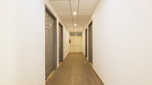 A narrow hallway with doors on both sides, a fire extinguisher on the wall, and a ceiling with recessed lighting. - Treebo Noida Express (Noida)