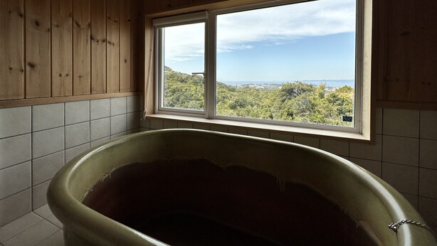 A bathroom with a bathtub, wooden walls, and a window with a view of a forest and distant landscape. - shirahamakashibessoD-157 (Shirahama)